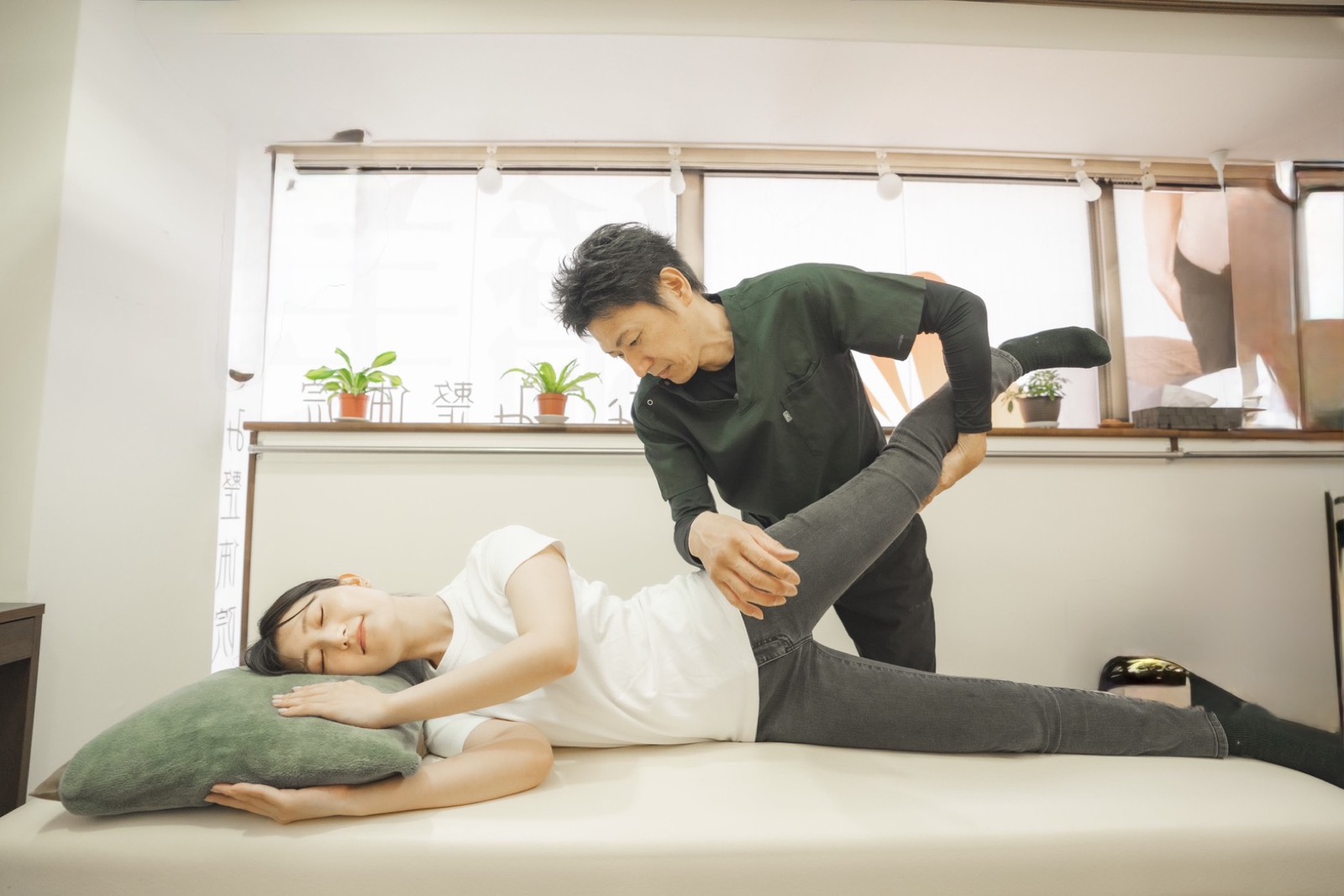 なごみ整骨院の院長が、横向きに寝たお客様の脚を持ち上げて股関節と腰の動きを確認している様子