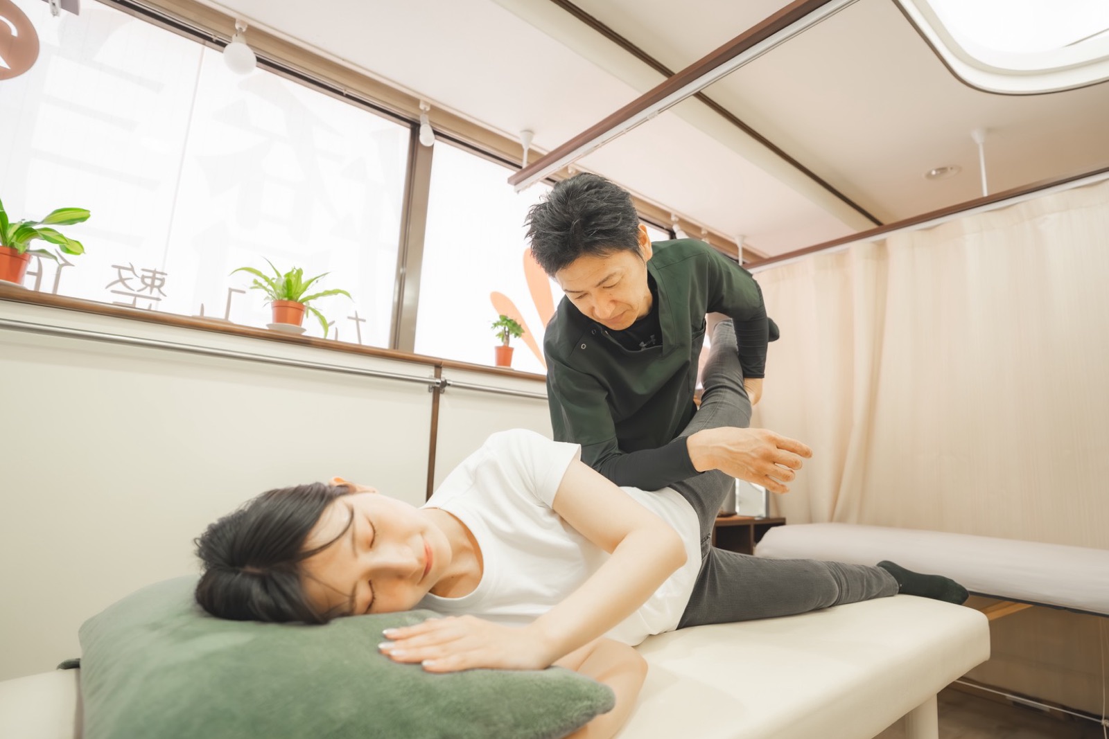 窓から光が入る明るい院内。院長がお客様の脚を支えながら施術している様子